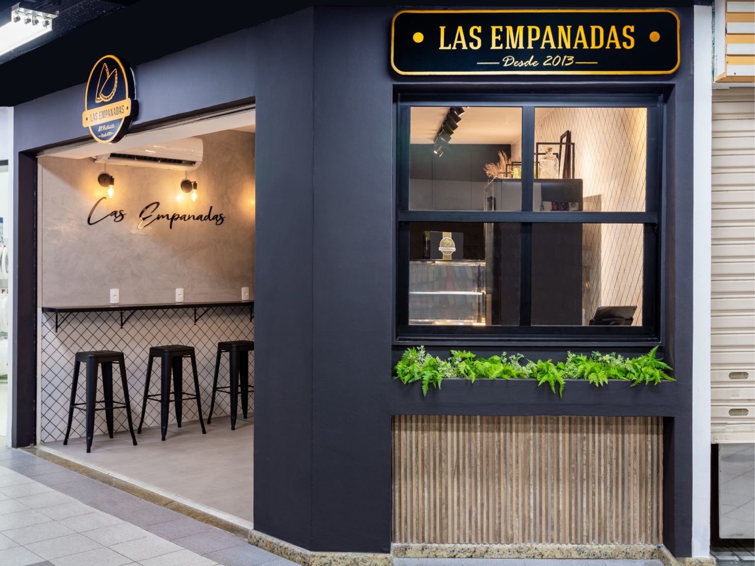 Fachada da loja Las Empanadas: letreiro dourado, vitrine e balcão com banquetas