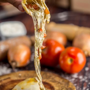 Empanada de queijo aberta, com o recheio derretido puxando, sobre tábua de madeira