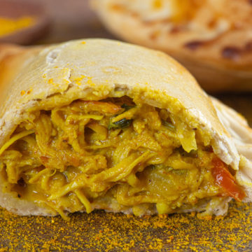 Empanada de frango ao curry aberta ao meio, mostrando o recheio desfiado